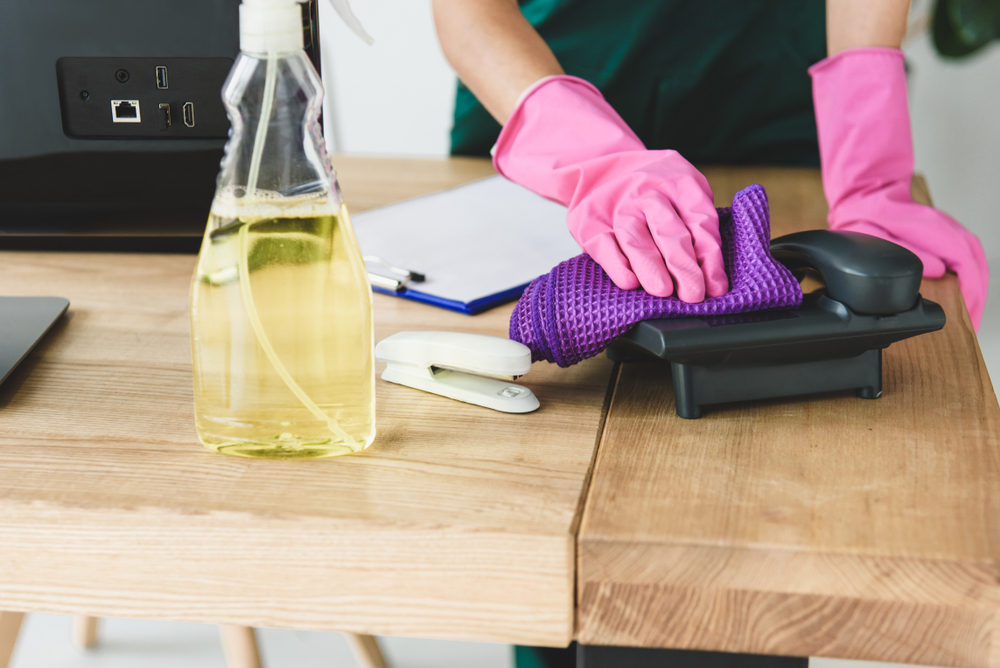 What Is Commercial Cleaning | someone cleaning a telephone on a work desk
